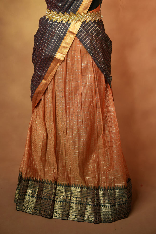 A traditional Indian saree displayed on a mannequin, featuring a peach-colored body with a metallic gold border and a dark navy blue and gold checkered drape.