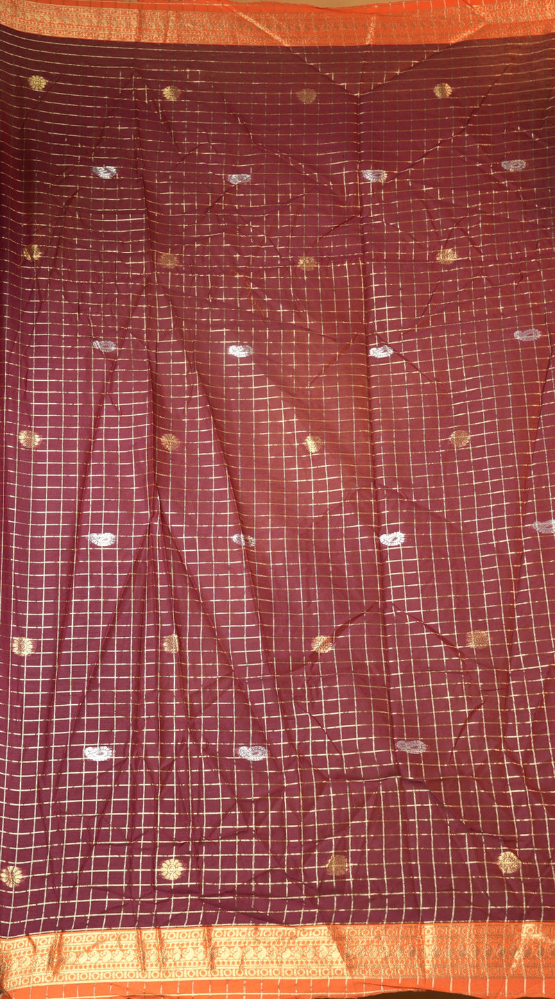 A close-up of a dark red or maroon fabric with a white grid pattern and scattered small gold and silver motifs, finished with a wide orange-gold border.