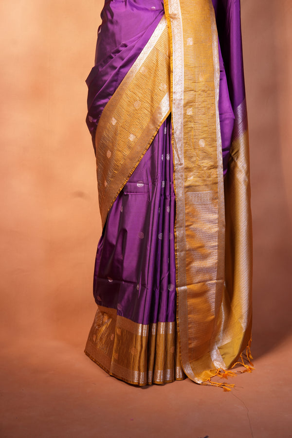 A folded purple and gold sari draped over a shelf against a warm peach-colored wall.