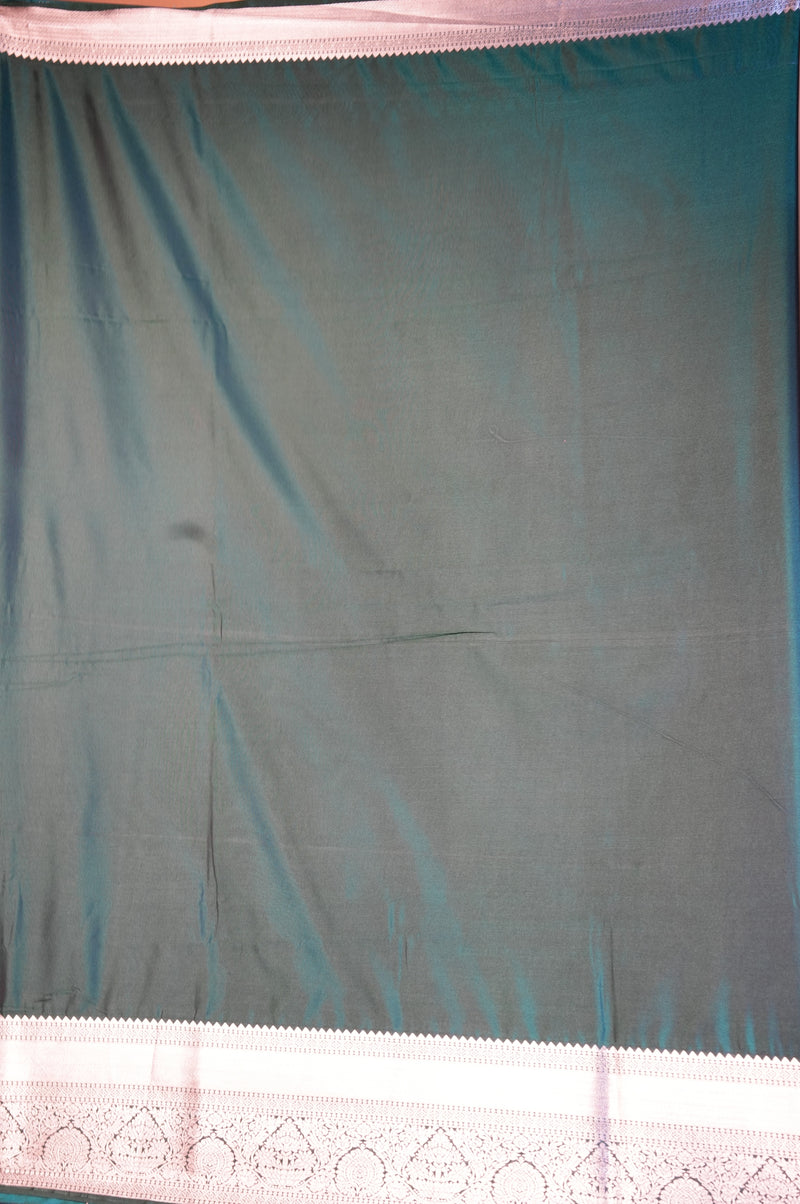 A dark teal-green fabric panel, likely a saree drape or curtain, featuring a light pink border with a scalloped edge and intricate floral embroidery along the bottom.