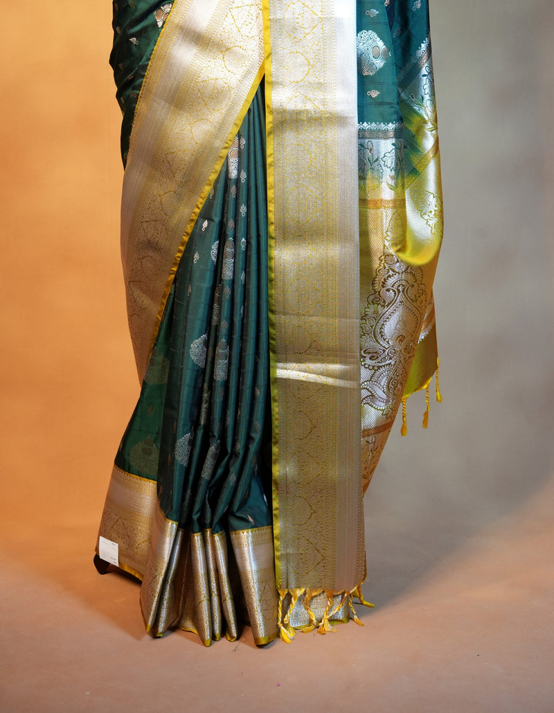 A close-up of a dark teal green silk saree with intricate gold zari embroidery, featuring a wide gold border and a matching gold and green pallu.