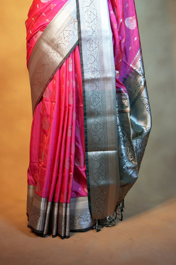 A folded pink and silver Banarasi silk saree with intricate zari work, displayed on a neutral surface.
