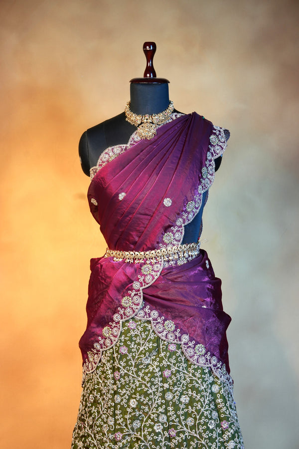 A traditional Indian sari displayed on a black mannequin. The sari features a rich magenta and purple gradient upper drape with intricate gold and silver floral embroidery, and a green lower skirt section heavily embellished with white floral patterns and gold borders.