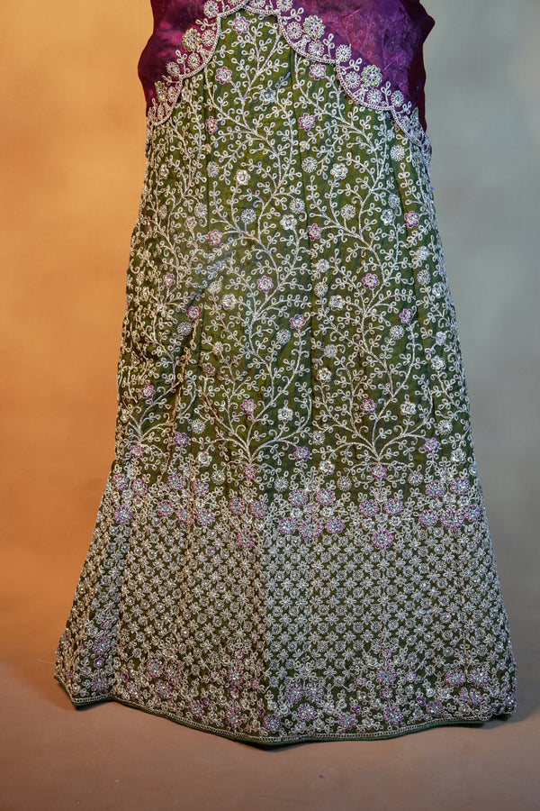An olive green embroidered skirt with intricate white floral vine patterns and purple accents, paired with a purple embroidered blouse, shown against a warm beige background.