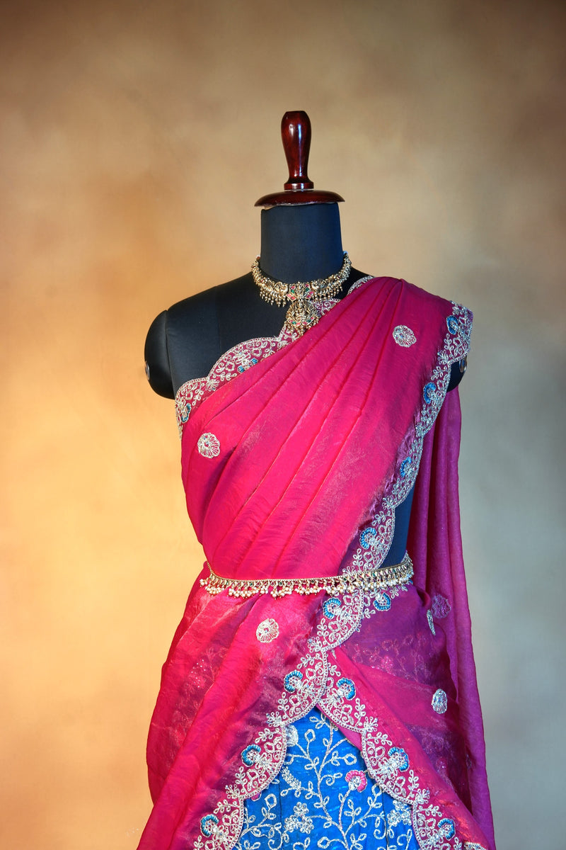A traditional Indian sari displayed on a black mannequin torso. The sari features a bright magenta-pink upper drape with silver and gold floral embroidery, a matching pink border, and a contrasting royal blue lower drape with white floral embroidery.