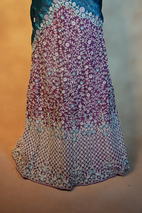 A close-up of a traditional embroidered fabric, likely part of a salwar suit, featuring a gradient design. The fabric transitions from a light beige and white floral pattern on the left, through a deep purple and magenta center with dense white embroidery, to a teal blue section on the right.
