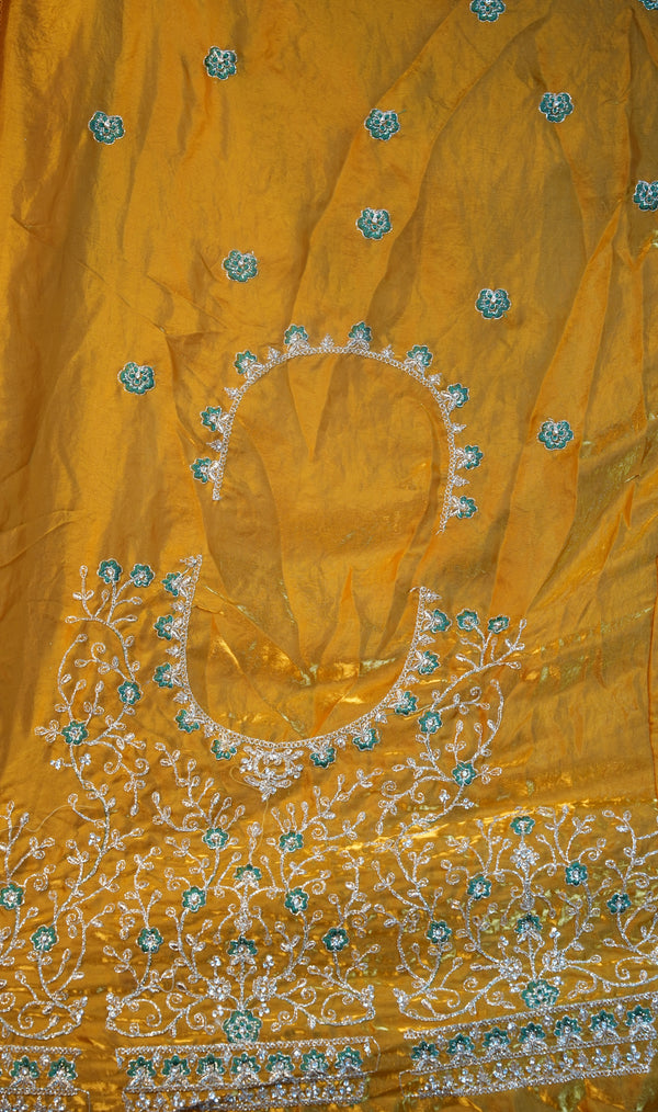 A close-up of a yellow embroidered fabric, likely part of a traditional ethnic outfit, featuring intricate silver and turquoise floral embroidery and beadwork.