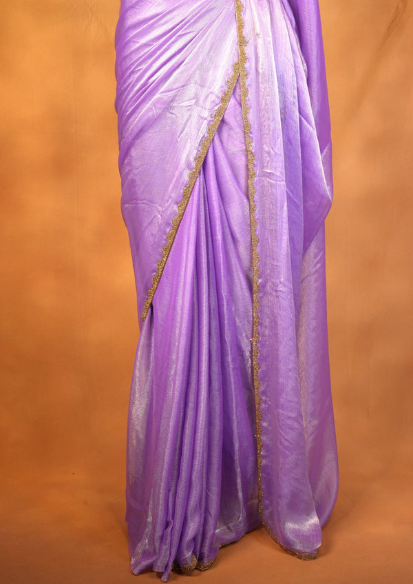 A draped purple sari with a shimmering finish and a thin gold border, shown against a solid warm brown background.