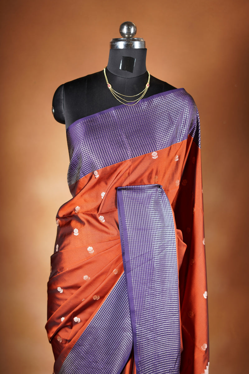 Luxury semi soft silk Banarasi weave saree in rust orange with lightweight drape and woven buti motifs. Features a contrast mauve border with subtle lurex shimmer and includes a matching contrast blouse for an elegant festive look.