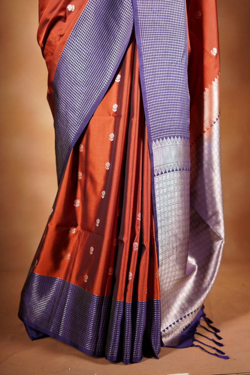 Luxury semi soft silk Banarasi weave saree in rust orange with lightweight drape and woven buti motifs. Features a contrast mauve border with subtle lurex shimmer and includes a matching contrast blouse for an elegant festive look.