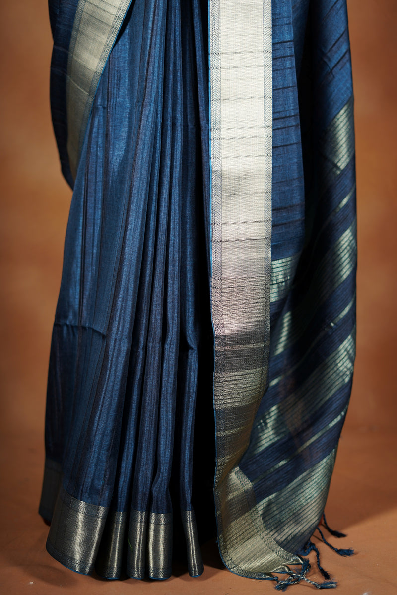 Dark slate blue Semi Tussar - Features a contrasting silver zari border and a grand pallu detailed with classic horizontal stripes and matching tassel fringe.