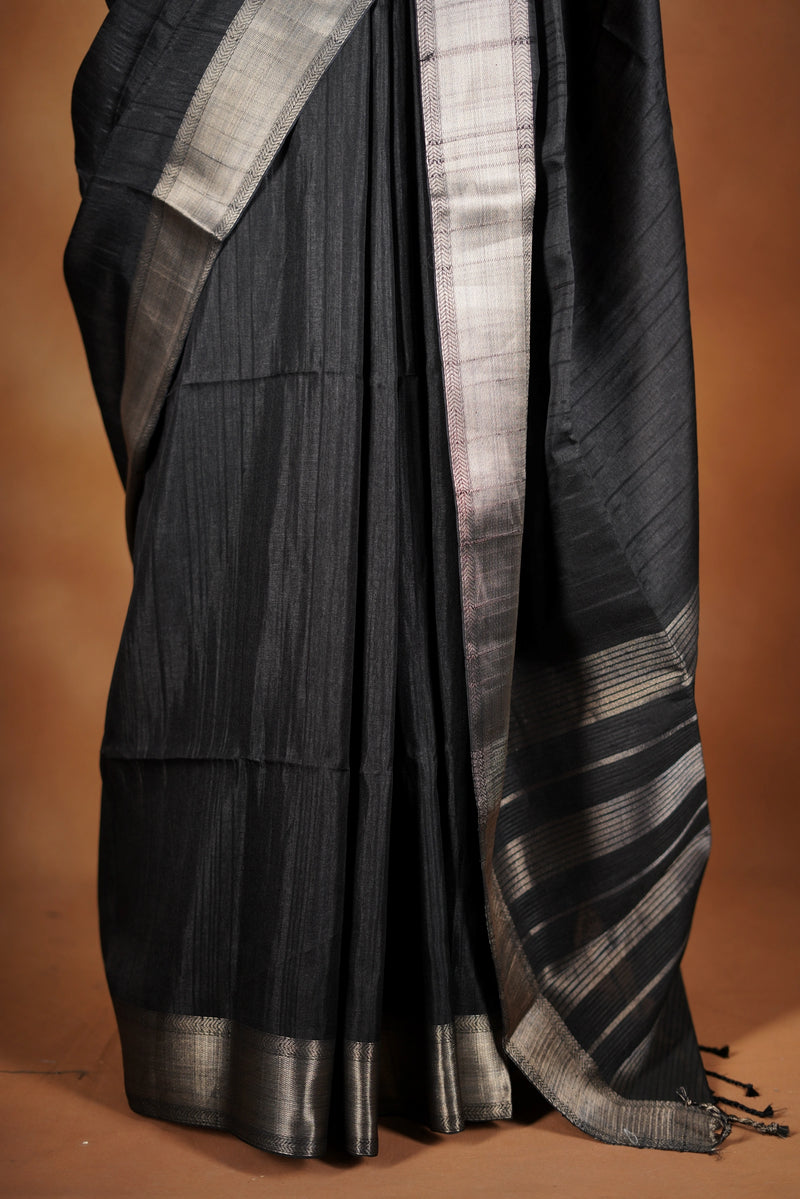 Fade Black Semi Tussar - designed to capture attention with its luxurious appeal. The vibrant tone is enhanced by delicate texture detailing and a lustrous zari border that adds depth and richness.