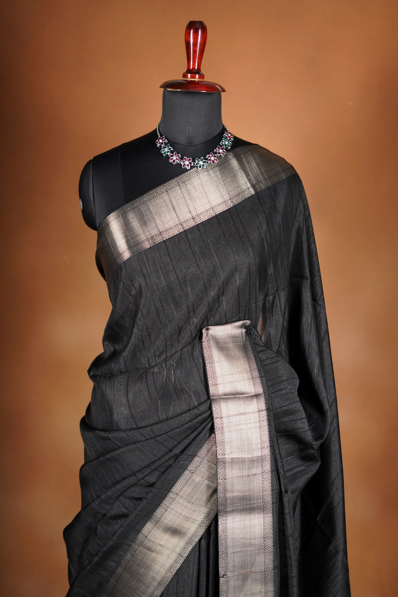 Fade Black Semi Tussar - designed to capture attention with its luxurious appeal. The vibrant tone is enhanced by delicate texture detailing and a lustrous zari border that adds depth and richness.