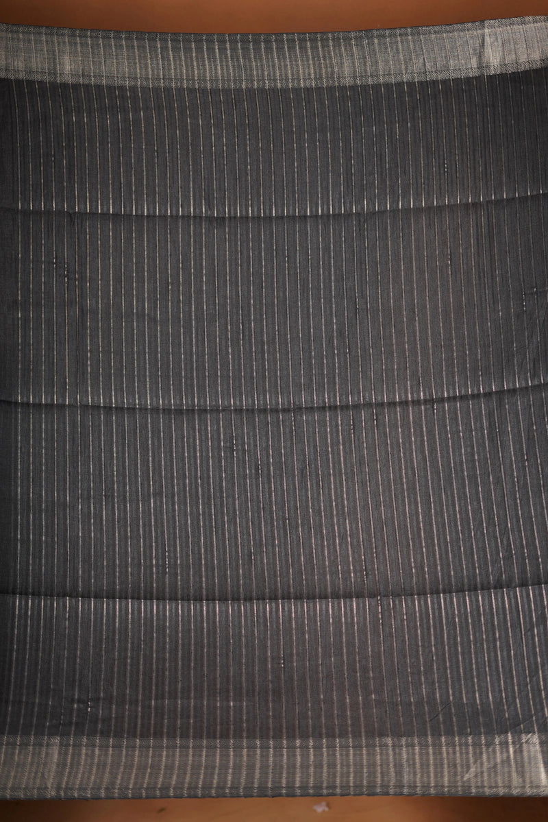 Fade Black Semi Tussar - designed to capture attention with its luxurious appeal. The vibrant tone is enhanced by delicate texture detailing and a lustrous zari border that adds depth and richness.