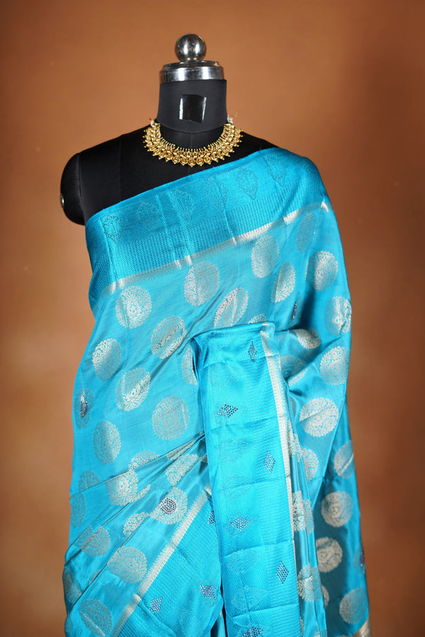 Aqua Blue Fancy semi jute saree - It features an elegant gold zari border with fine woven detailing and a matching zari pallu. The body has small round gold butta motifs, evenly spread for a subtle  traditional look with a matching blouse.