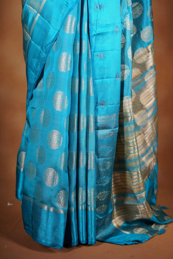 Aqua Blue Fancy semi jute saree - It features an elegant gold zari border with fine woven detailing and a matching zari pallu. The body has small round gold butta motifs, evenly spread for a subtle  traditional look with a matching blouse.