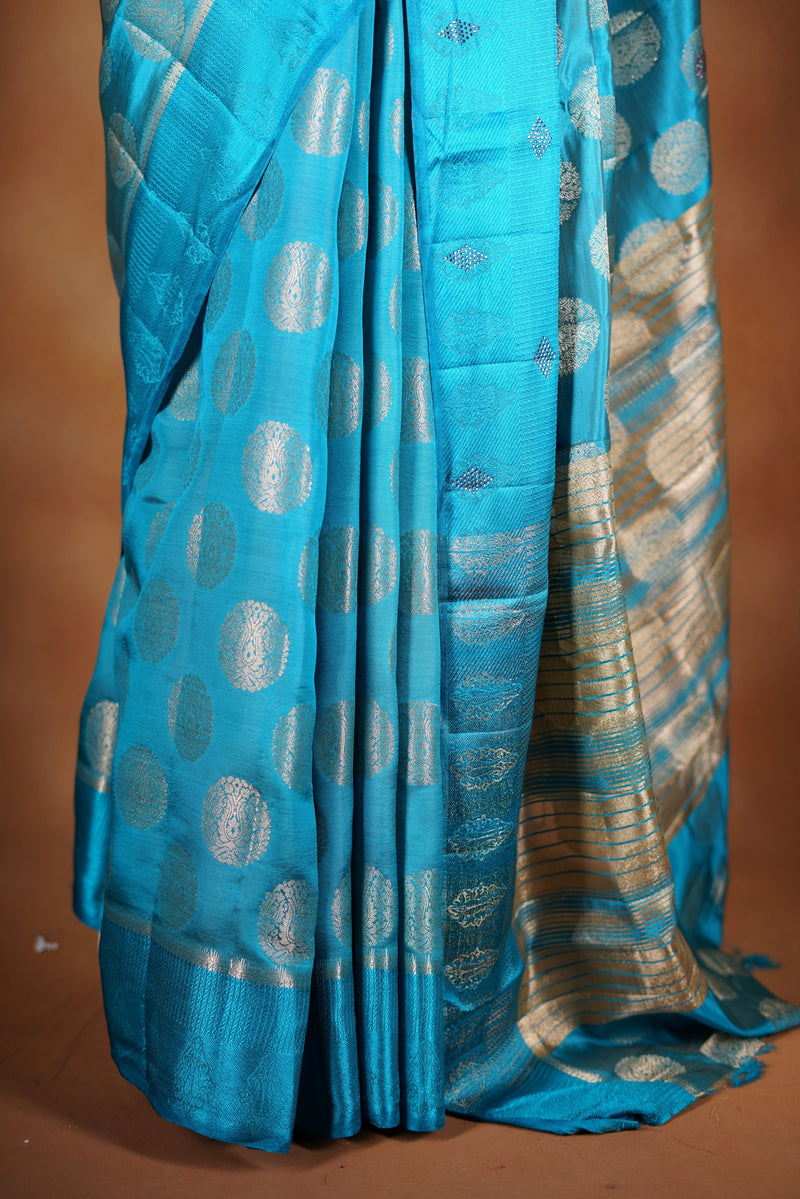 Aqua Blue Fancy semi jute saree - It features an elegant gold zari border with fine woven detailing and a matching zari pallu. The body has small round gold butta motifs, evenly spread for a subtle  traditional look with a matching blouse.
