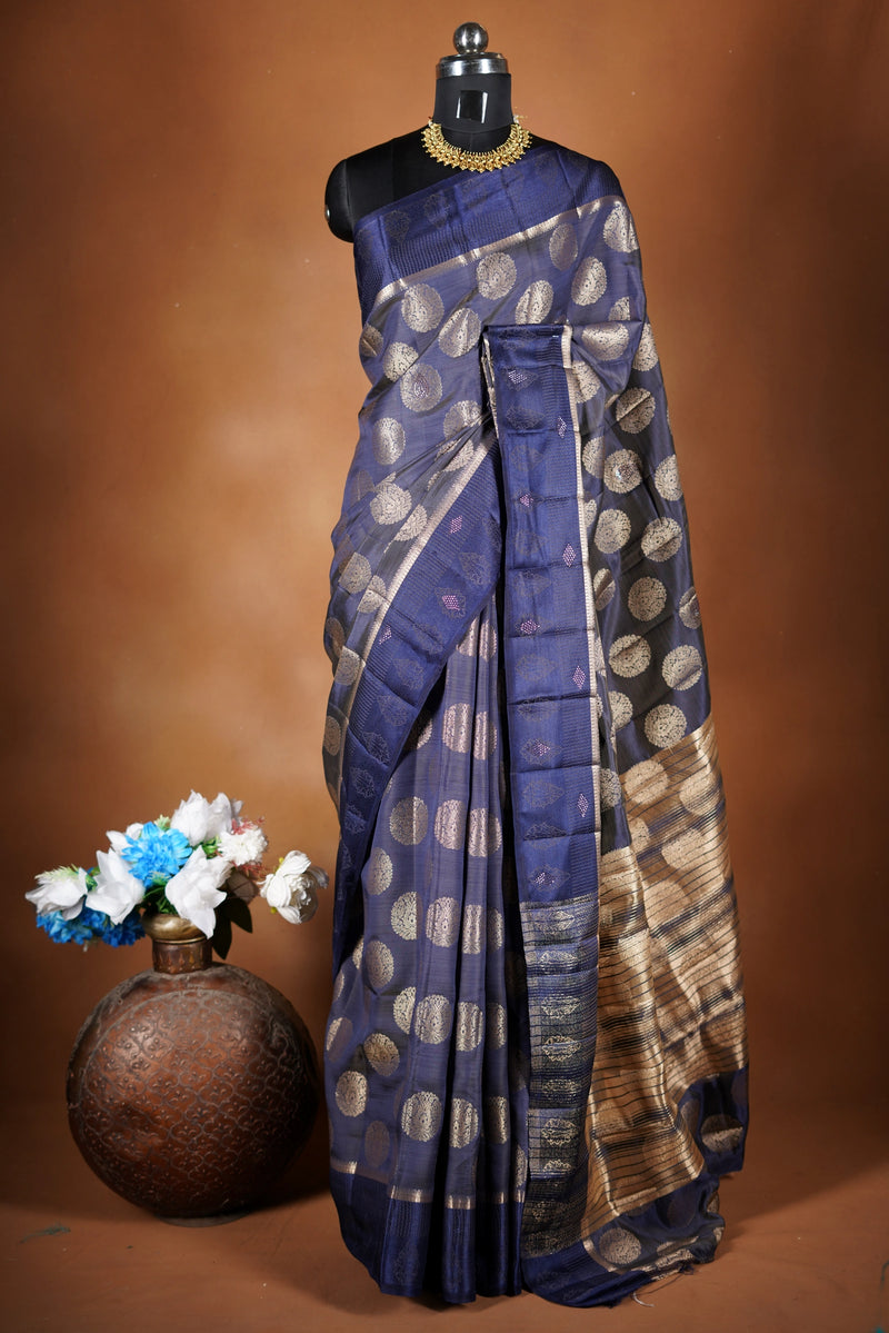 Navy blue Fancy semi jute saree - It features an elegant gold zari border with fine woven detailing and a matching zari pallu. The body has small round gold butta motifs, evenly spread for a subtle, graceful traditional look with a matching blouse.