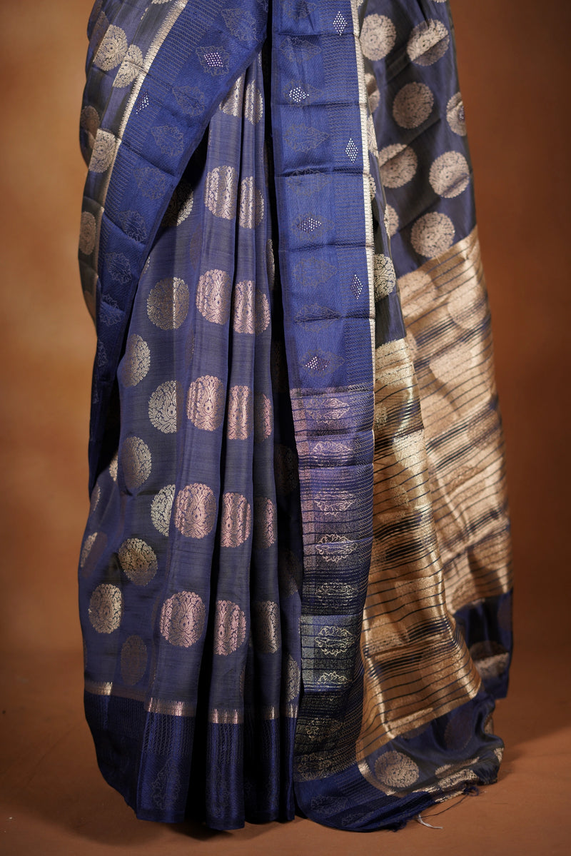 Navy blue Fancy semi jute saree - It features an elegant gold zari border with fine woven detailing and a matching zari pallu. The body has small round gold butta motifs, evenly spread for a subtle, graceful traditional look with a matching blouse.