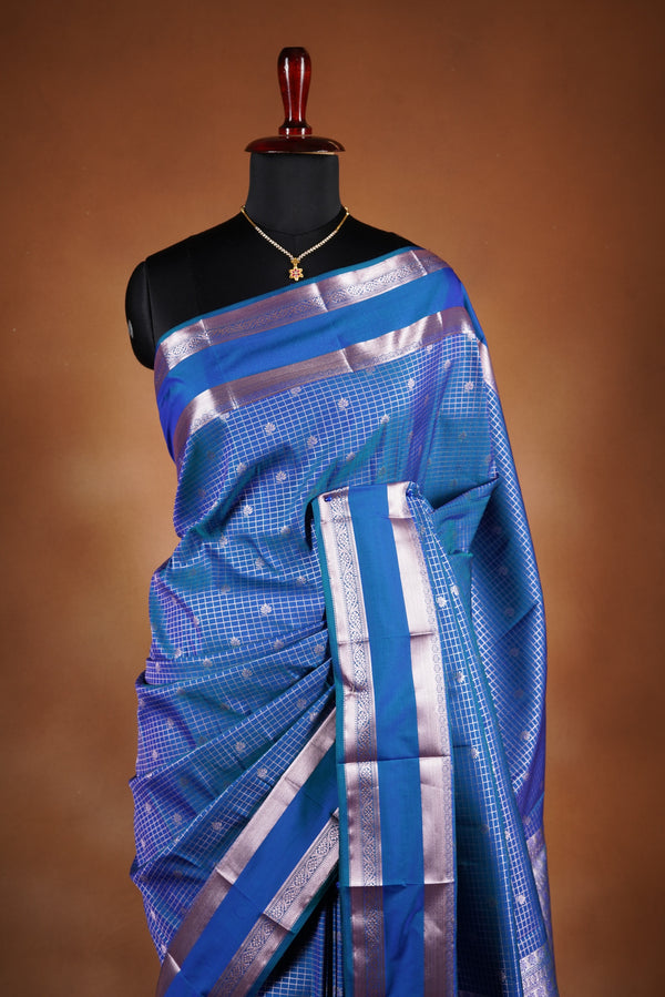 Royal blue soft silk saree featuring a modern checkered body design with elegant silver zari border and striped pallu. Lightweight and graceful, it blends contemporary geometric style with traditional elegance.