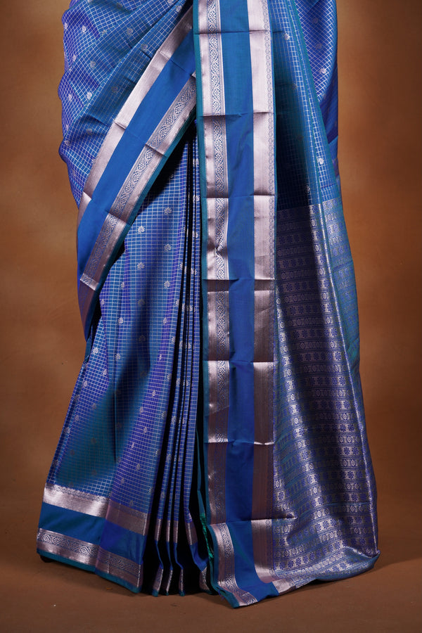 Royal blue soft silk saree featuring a modern checkered body design with elegant silver zari border and striped pallu. Lightweight and graceful, it blends contemporary geometric style with traditional elegance.