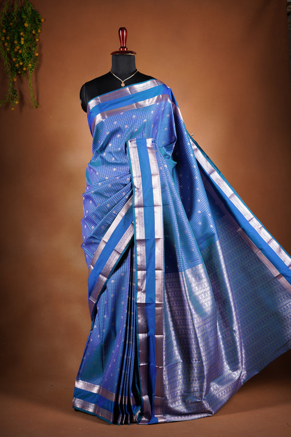 Royal blue soft silk saree featuring a modern checkered body design with elegant silver zari border and striped pallu. Lightweight and graceful, it blends contemporary geometric style with traditional elegance.