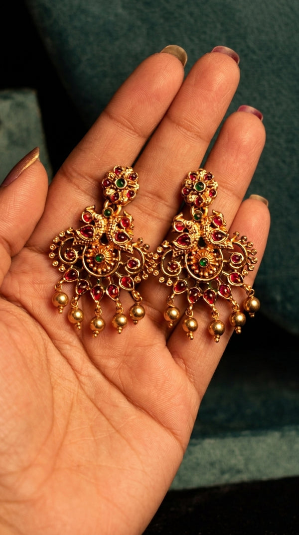 Ornate gold earrings with gemstones held in a hand against a dark background
