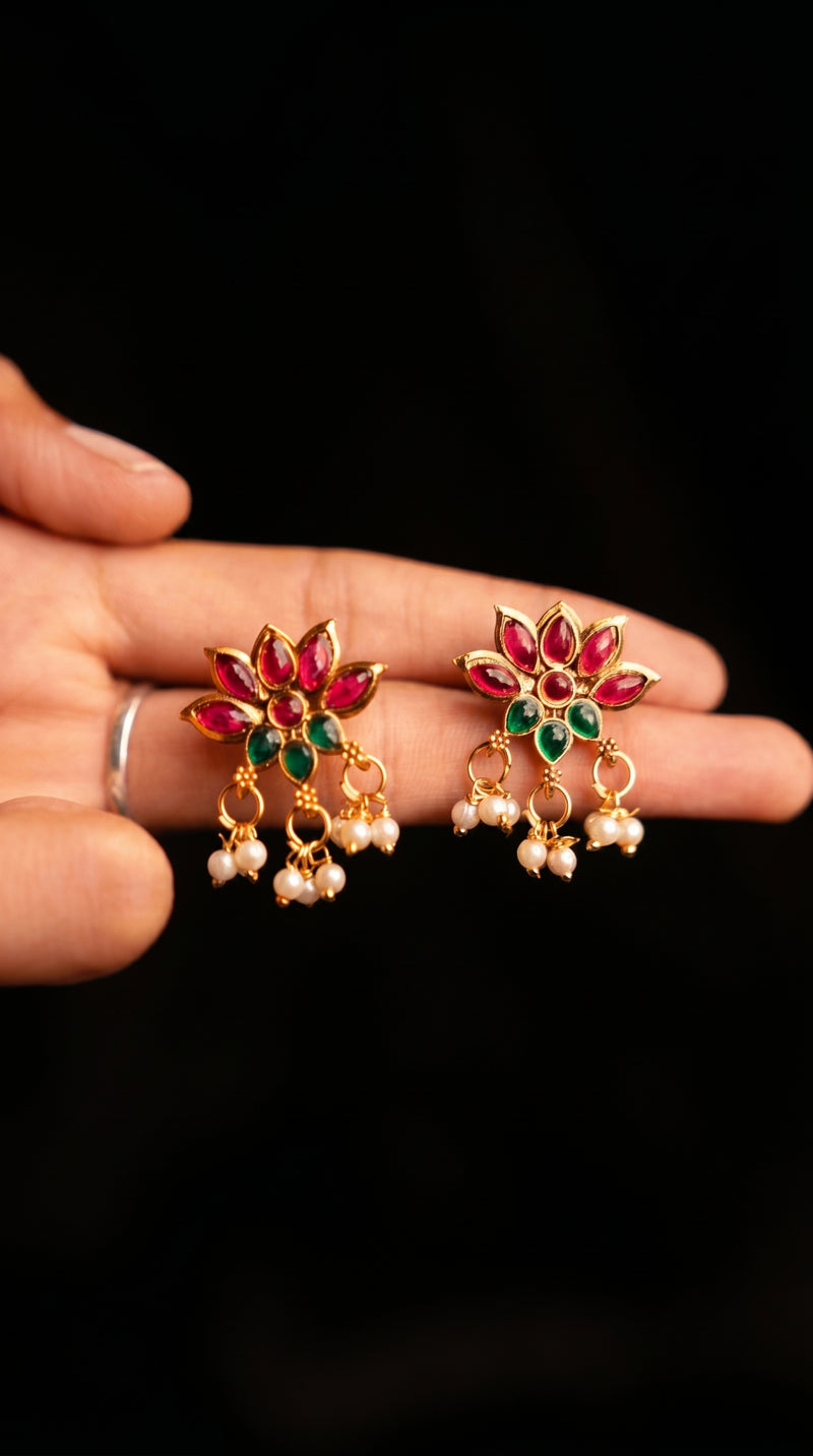 Decorative earrings with gemstones and pearls held in a hand against a black background