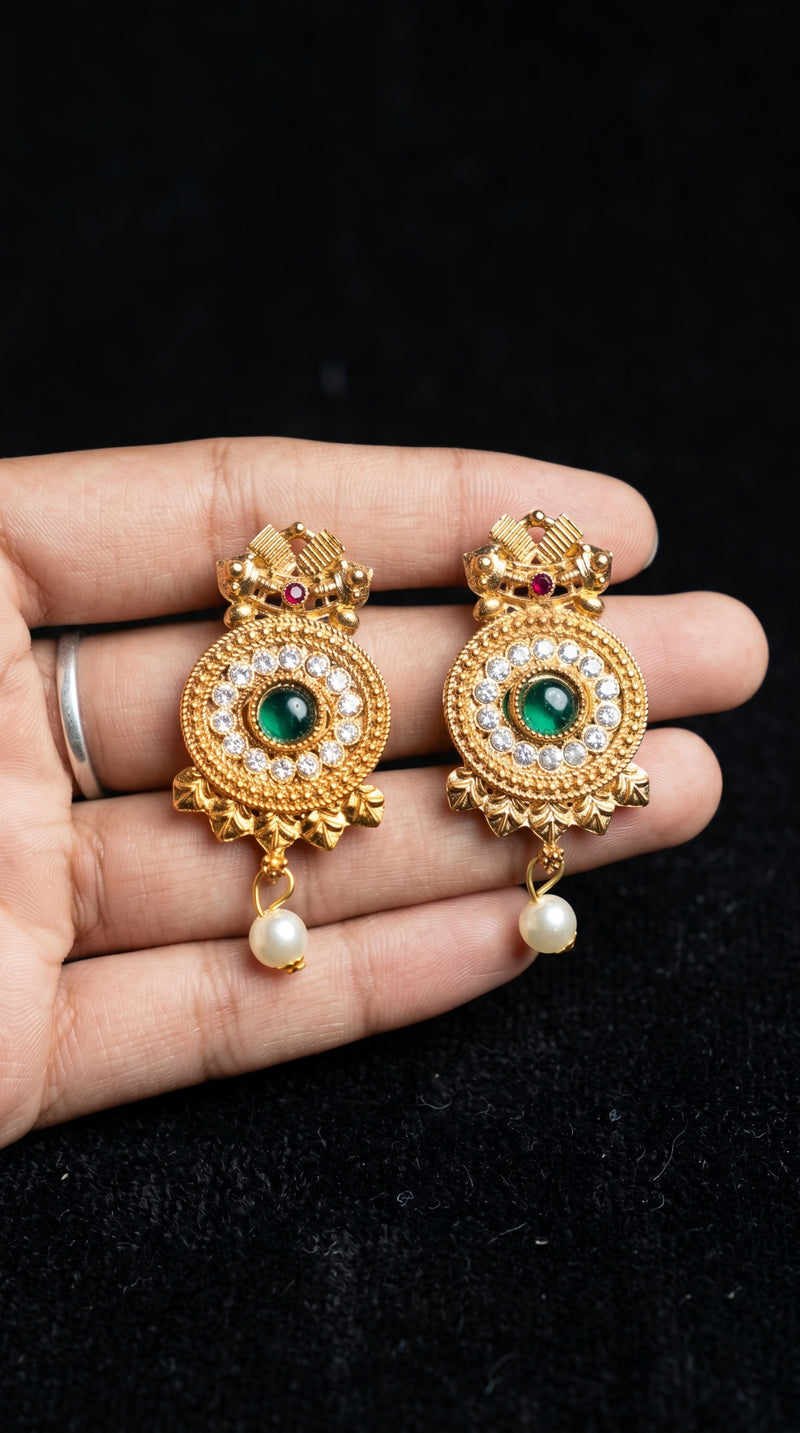 Gold earrings with green gemstones and pearls held in a hand against a black background