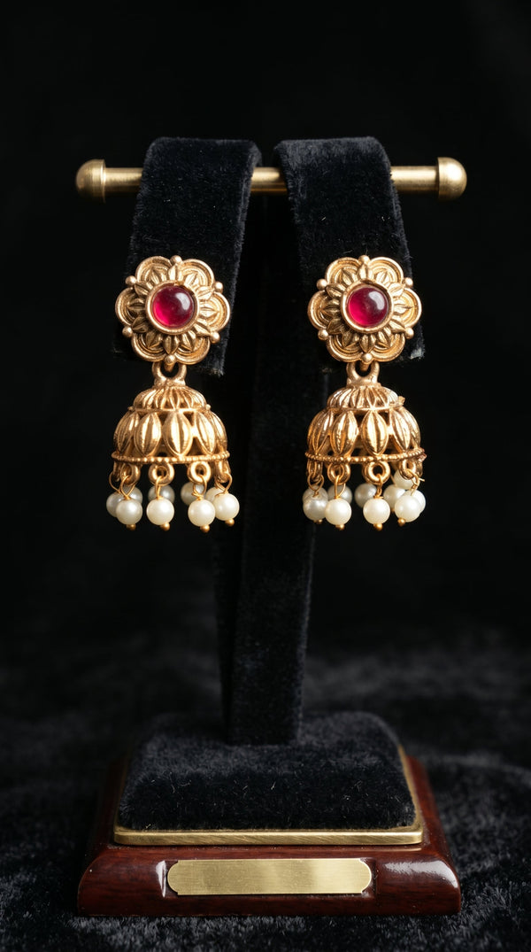 Gold earrings with red gemstones and pearl-like beads on a black stand.