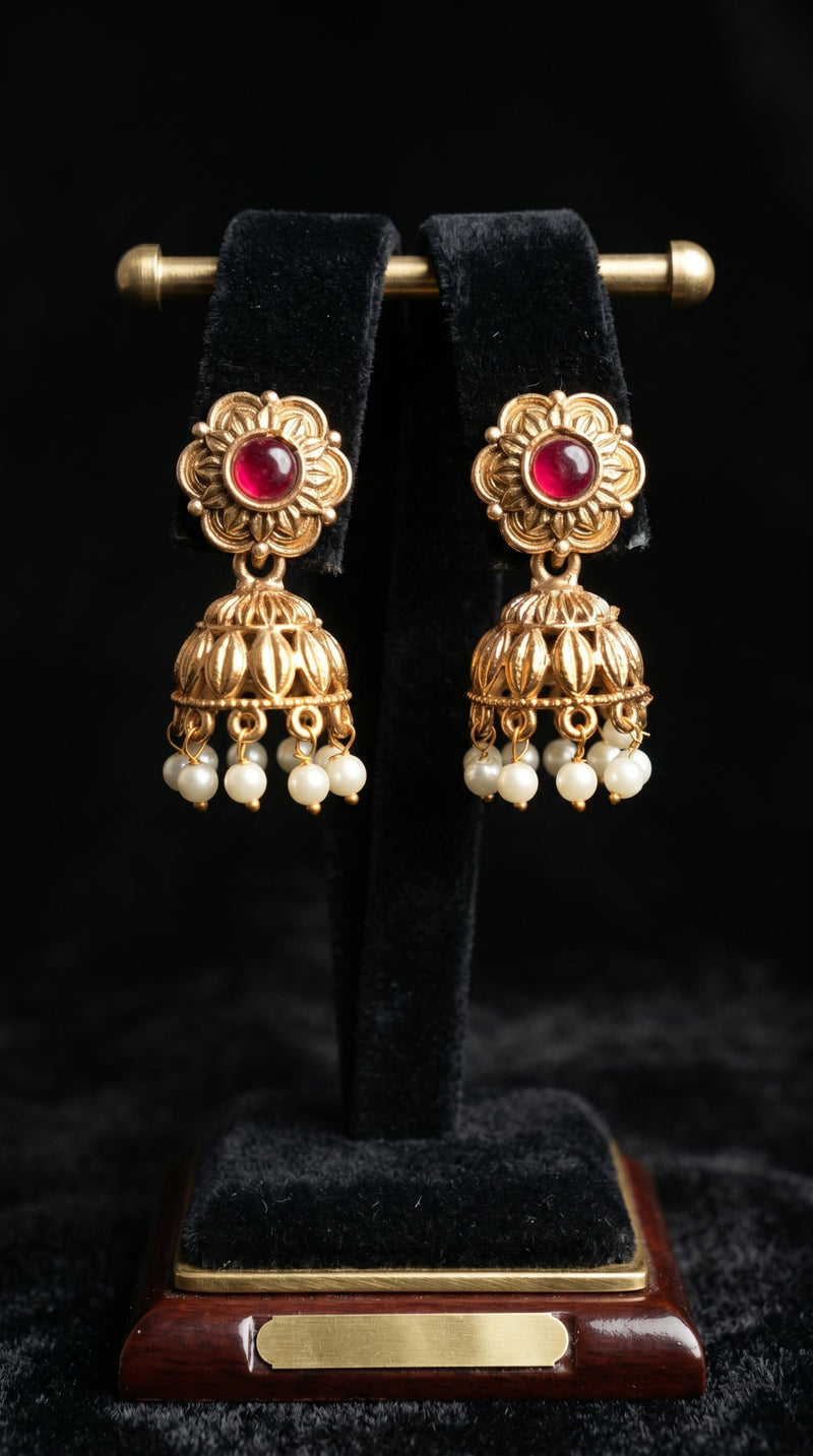Gold earrings with red gemstones and pearl-like beads on a black stand.
