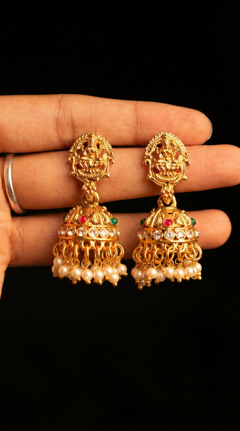 Gold earrings with pearls and gemstones held between fingers against a black background