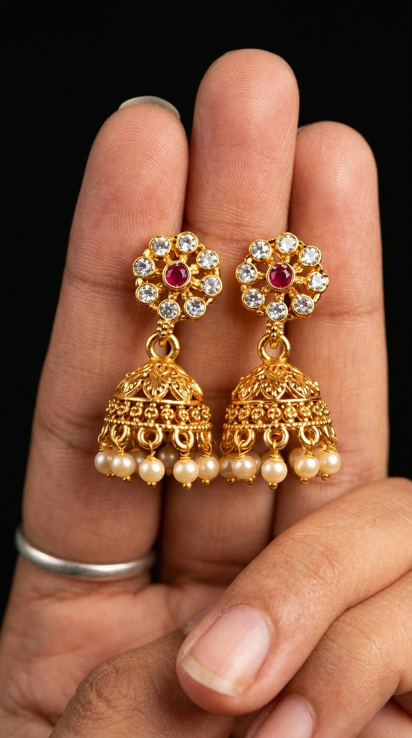 Gold earrings with pearls and red stones held between fingers against a dark background