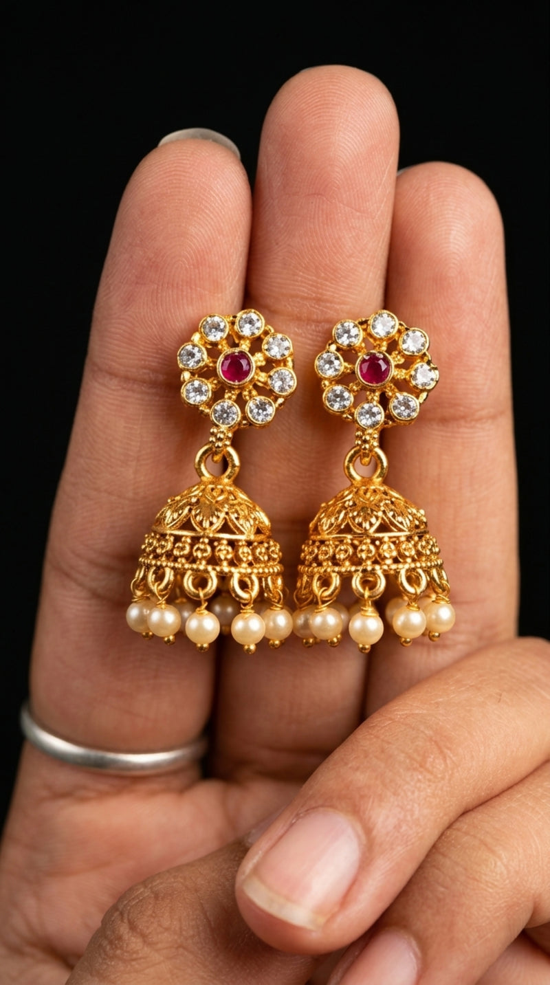 Gold earrings with pearls and red stones held between fingers against a dark background