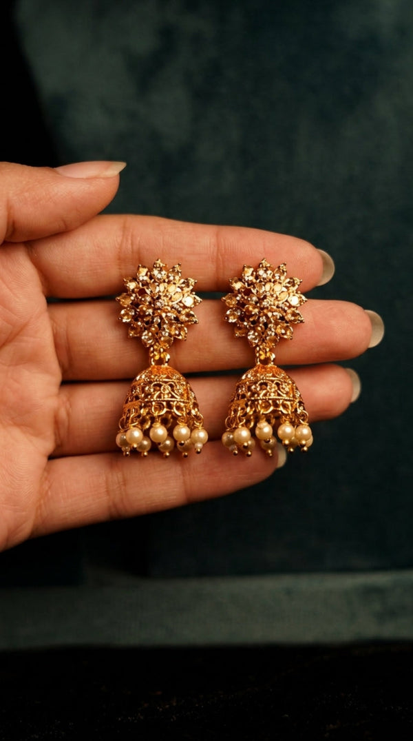 Gold earrings held in a hand against a dark background