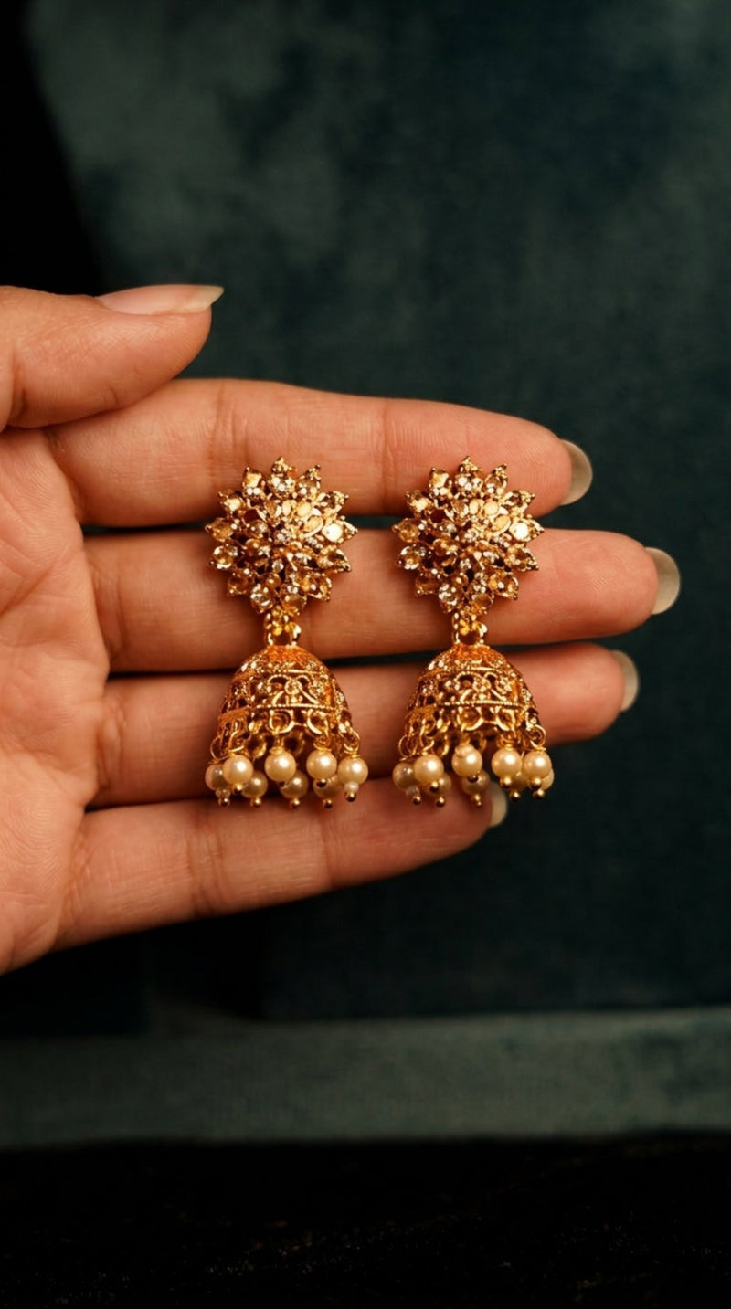 Gold earrings held in a hand against a dark background