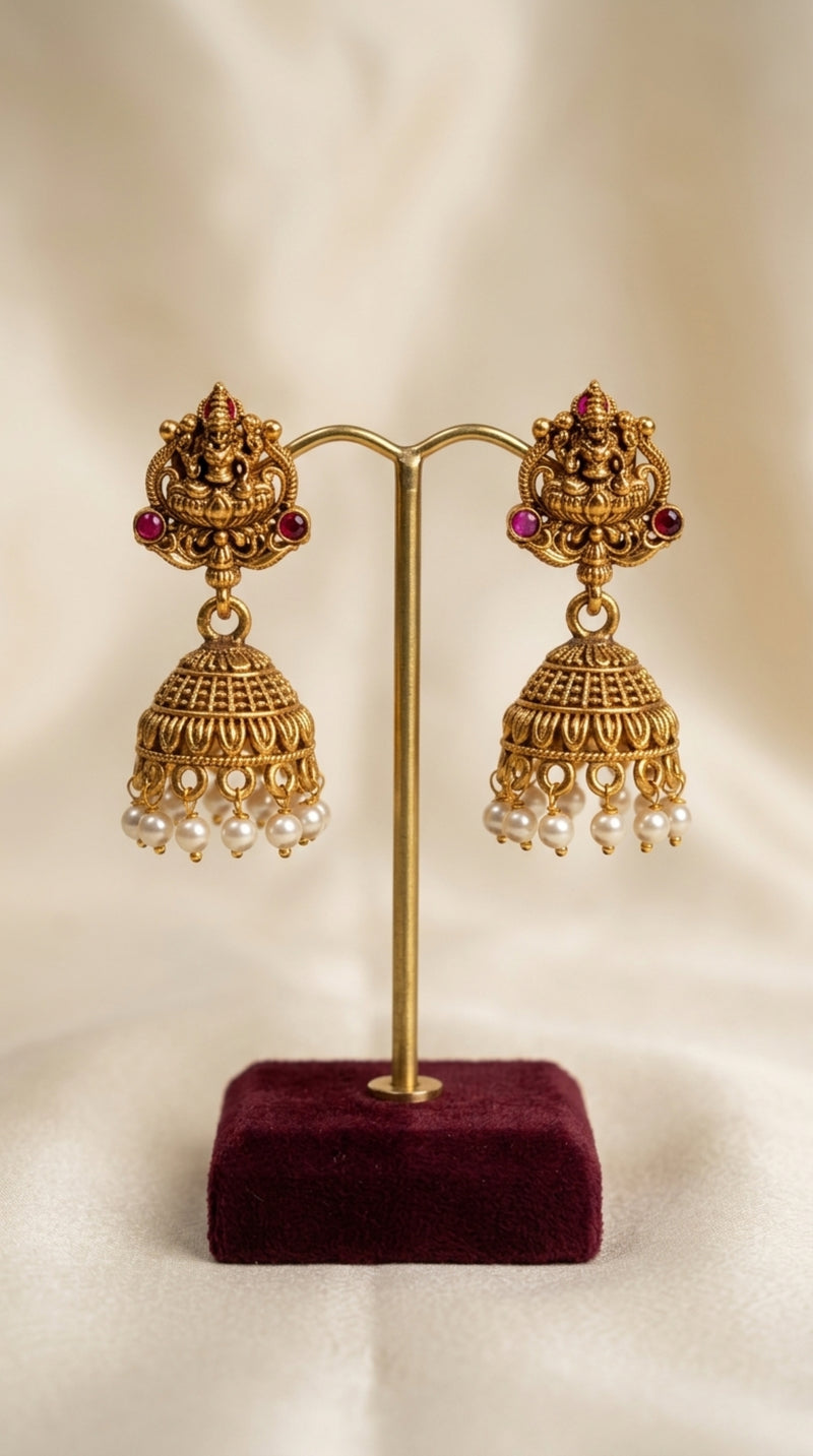 Gold earrings on a stand with a beige background