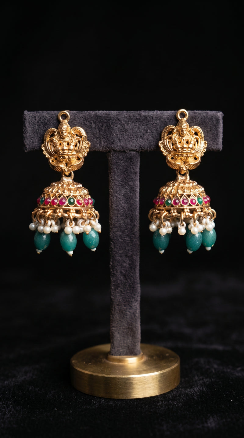 Antique gold Lakshmi jhumka earrings featuring multicolor ruby and emerald stones, pearl accents, and green bead drops in traditional South Indian temple jewellery design.