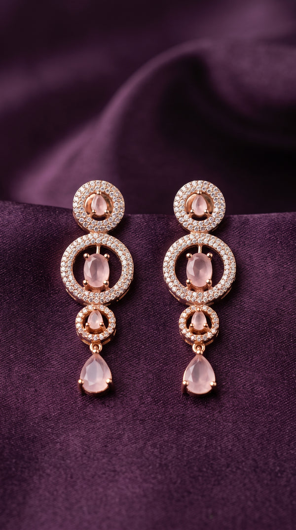 Pair of gold earrings with pink gemstones on a purple fabric background