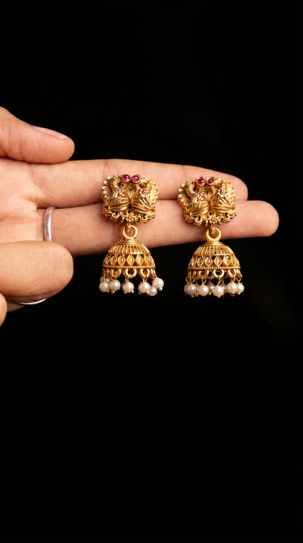 Gold earrings with pearl drops held by a hand against a black background