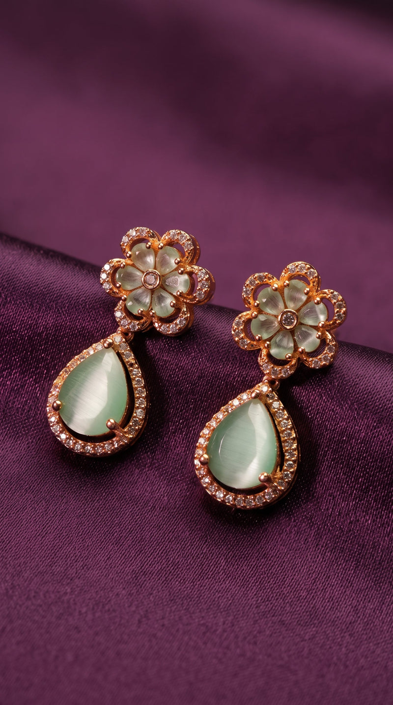 Pair of earrings with green gemstones and gold accents on a purple fabric background