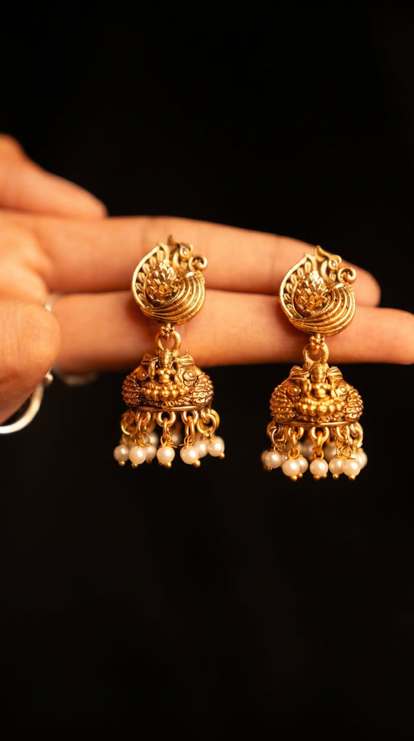 Gold earrings with pearl drops held by a hand against a black background