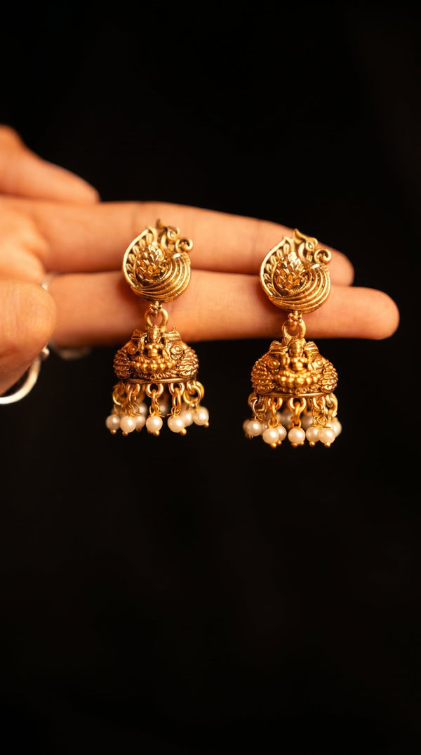 Gold earrings with pearl drops held by a hand against a black background
