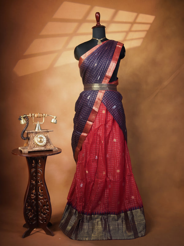 A traditional Indian saree displayed on a black mannequin, featuring a deep red skirt with a dark purple border, a matching dark purple blouse, and a decorative antique-style rotary phone on a carved side table against a warm brown backdrop.