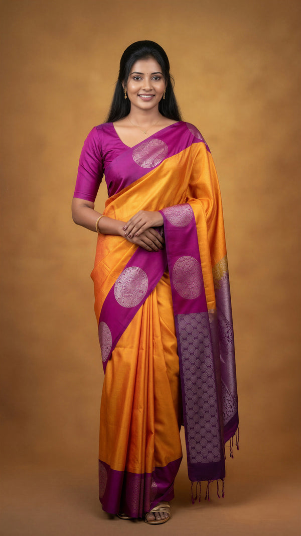 A woman modeling a traditional Indian saree with a bright orange body, purple border, and purple blouse, set against a solid brown studio backdrop.