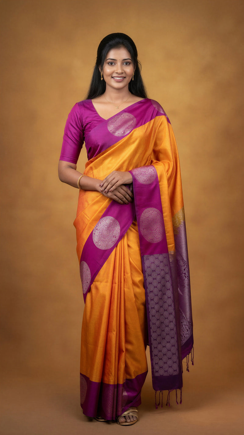 A woman modeling a traditional Indian saree with a bright orange body, purple border, and purple blouse, set against a solid brown studio backdrop.