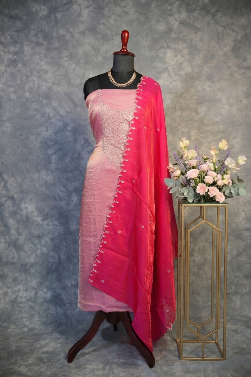 Mannequin wearing a pink saree with a red border, standing next to a small table with flowers against a gray background.