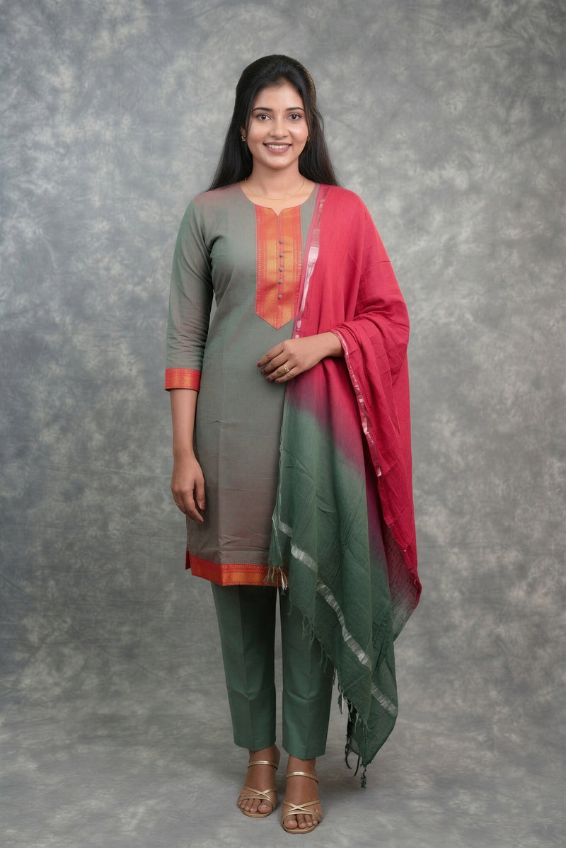 A woman modeling a traditional Indian salwar kameez suit set. The outfit features a muted gray-green kameez kurta with orange embroidery and a matching dupatta that has a red-to-green gradient with subtle silver patterns, paired with matching trousers.