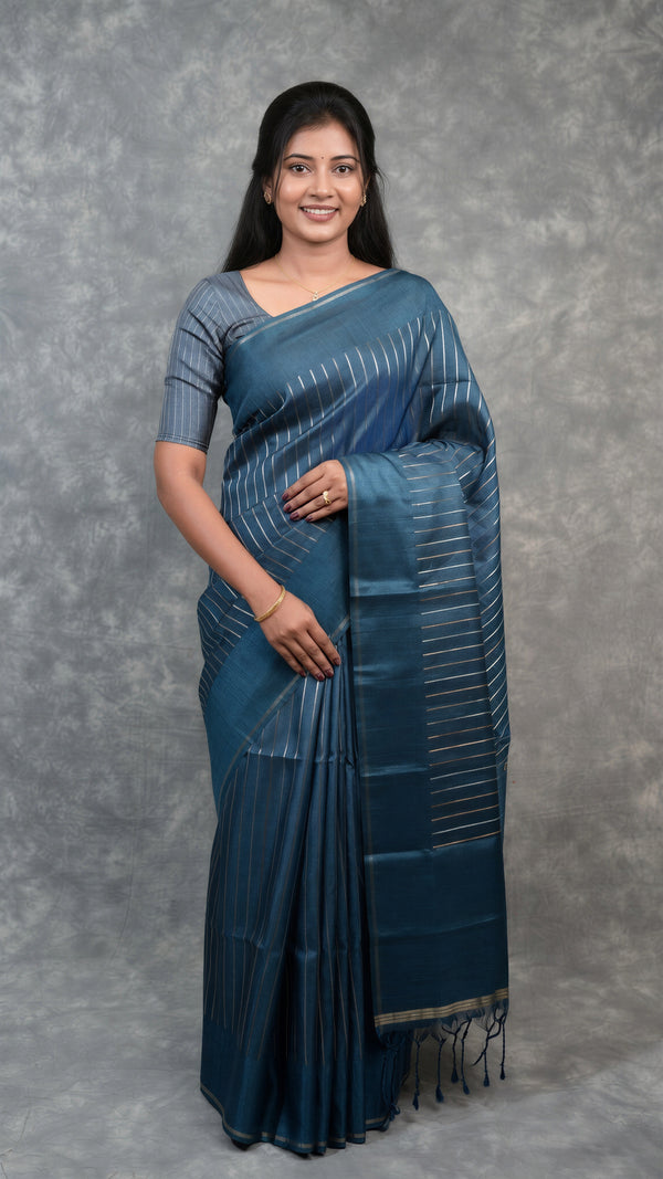 A woman modeling a dark blue saree with subtle vertical stripes and a matching blouse, standing against a textured gray backdrop.