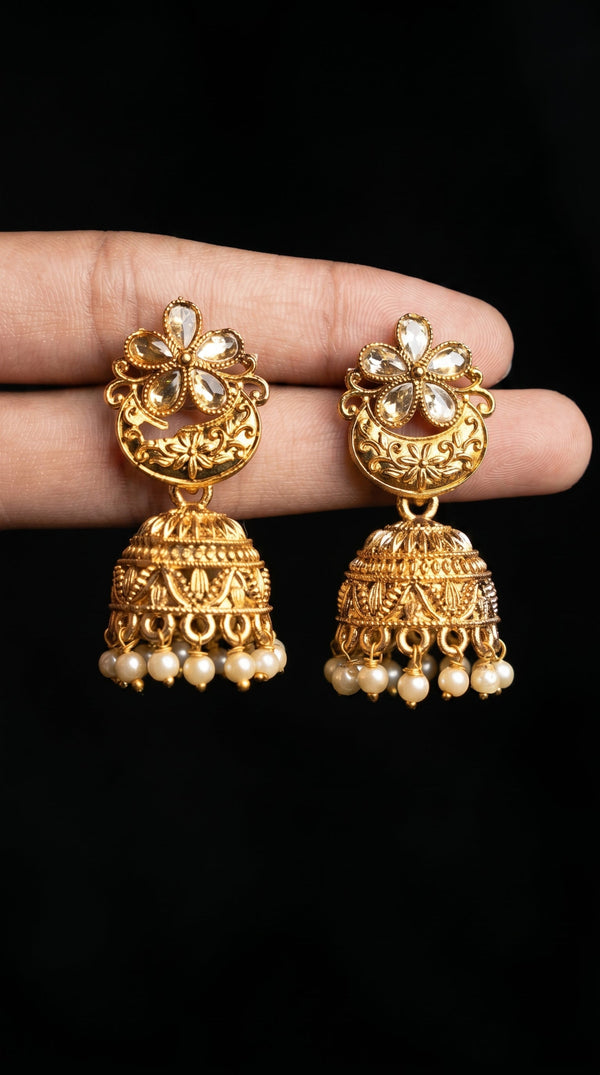 Gold earrings with pearl drops held between fingers against a black background